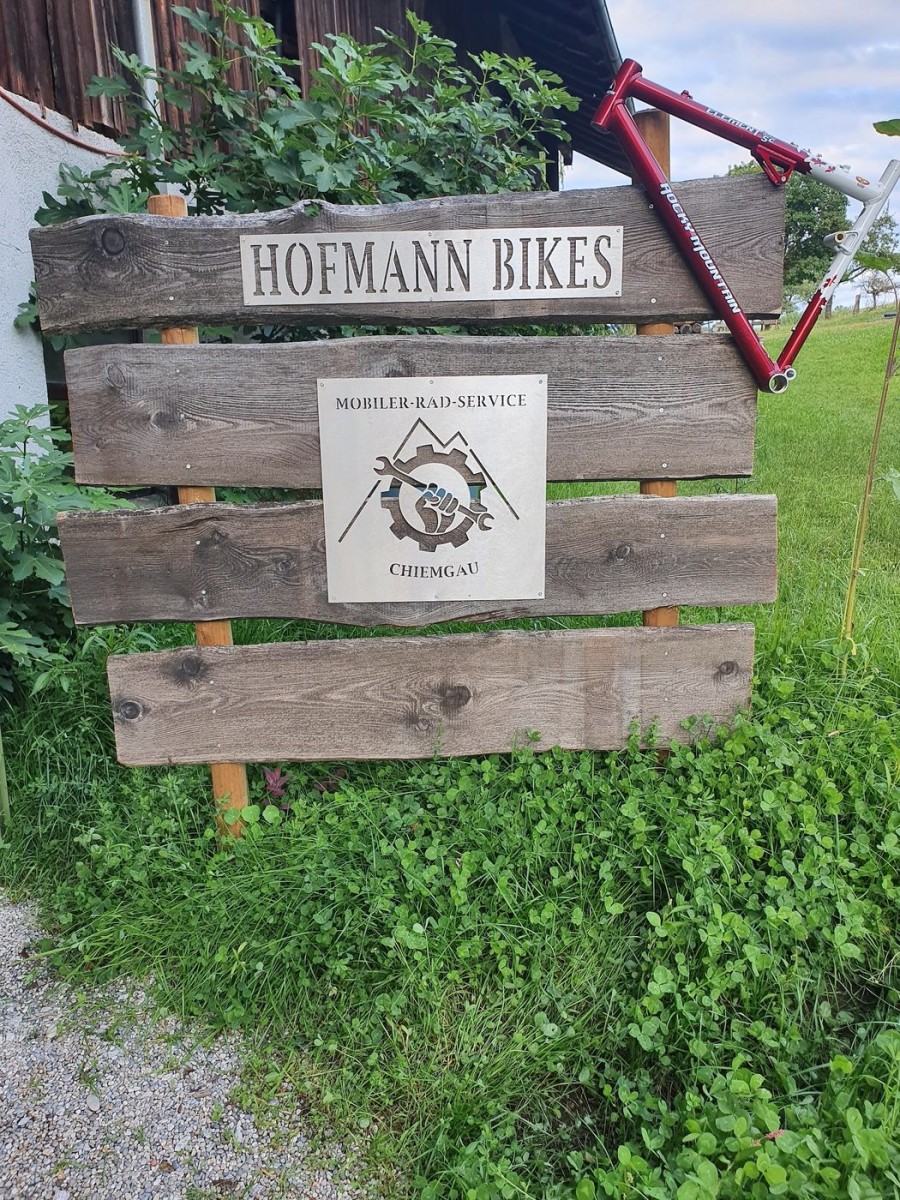 Holzschild am Hof in Thalham mit dem Logo von Hofmann Bikes und der Zeile „Mobiler Rad-Service Chiemgau".